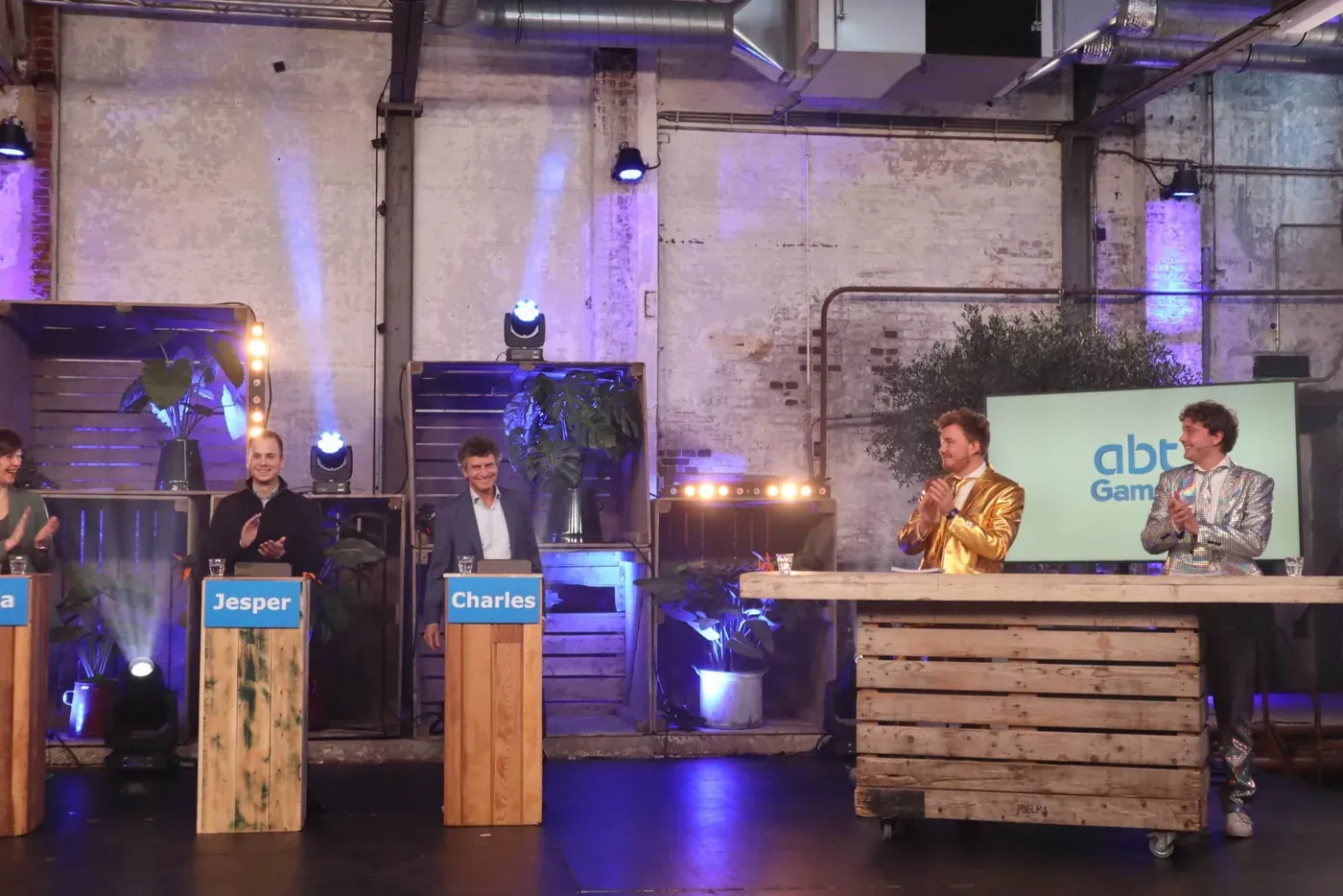 Kenneth en Andor presenteren de Pubquiz Show op een podium met teamnamen en schermen